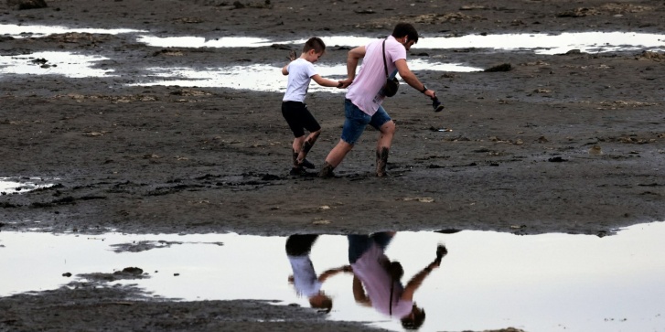 Κάτοικοι της Ζαπορίζια περπατούν μέσα στη λάσπη του ποταμού Δνείπερου, στις 10 Ιουνίου 2023, μετά τις ζημιές που υπέστη το φράγμα του υδροηλεκτρικού σταθμού Κακόβκα.