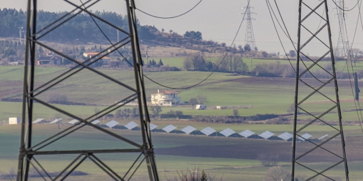 Ηλεκτρικοί πυλώνες υψηλής τάσης κοντά στην πόλη της Θεσσαλονίκης που παρέχουν ενέργεια από λιγνιτικούς σταθμούς στην περιοχή της Πτολεμαΐδας και της Κοζάνης, με κάποιους ηλιακούς συλλέκτες στο βάθος. [Νικόλας Οικονόμου/NurPhoto]