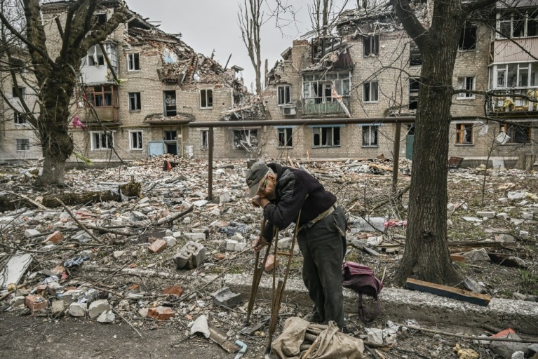 Ένας ηλικιωμένος άνδρας μαζεύει ξύλα από τα συντρίμμια μπροστά από μια κατεστραμμένη πολυκατοικία μετά από χτύπημα στην πόλη Αβντίιβκα της περιφέρειας Ντονέτσκ, στις 18 Μαρτίου 2023. [Aris Messinis/AFP]