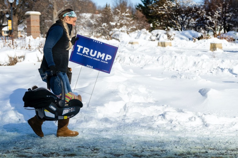 Μια υποστηρίκτρια του Ντόναλντ Τραμπ κουβαλάει ένα μωρό και ένα πλακάτ του Τραμπ καθώς αψηφά τις θερμοκρασίες κάτω από το μηδέν για να παρευρεθεί σε μια συγκέντρωση στην Ιντιανόλα της Άιοβα, στις 14 Ιανουαρίου 2024. [Jim WATSON/AFP]