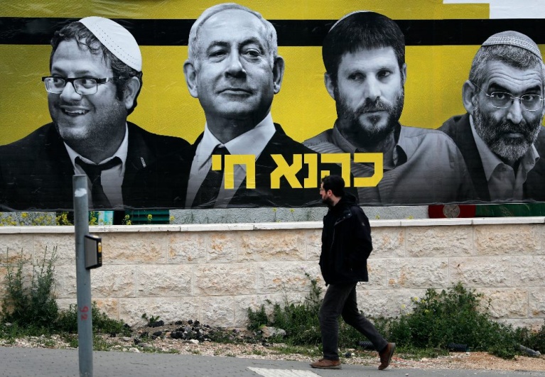Ένας Ισραηλινός περνά μπροστά από μια προεκλογική αφίσα που απεικονίζει τον πρωθυπουργό Μπέντζαμιν Νετανιάχου, πλαισιωμένο από τους ακροδεξιούς πολιτικούς Ιταμάρ Μπεν Γκβίρ, Μπεζαλέλ Σμοτρίχ και Μιχαήλ Μπεν Άρι, με τη λεζάντα στα εβραϊκά «Ο Καχάνα ζει», σε αναφορά σε ένα απαγορευμένο υπερεθνικιστικό κόμμα του 1994, στην Ιερουσαλήμ, στις 29 Μαρτίου 2019. Οι γενικές εκλογές στο Ισραήλ θα διεξαχθούν στις 9 Απριλίου 2019. (Φωτογραφία: THOMAS COEX / AFP)
