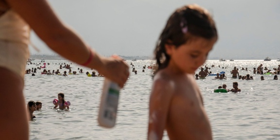 Γυναίκα βάζει αντιηλιακό σε παιδί σε παραλία της Σικελίας. [Roberto Boccaccino]
