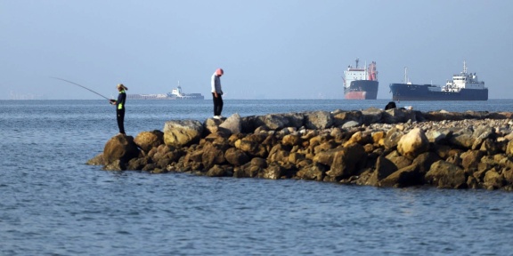 Σε αυτή τη φωτογραφία που προέρχεται από το ιρανικό πρακτορείο ειδήσεων ISNA, κάτοικοι ψαρεύουν από την ακτή, ενώ φορτηγά και εμπορικά πλοία βρίσκονται αγκυροβολημένα στο Στενό του Ορμούζ, ανοιχτά του Μπαντάρ Αμπάς, στις 8 Ιουνίου 2026. [AMIRHOSSEIN KHORGOOEI / ISNA / AFP]